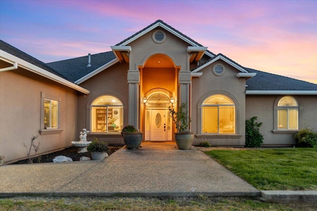 view of exterior entry featuring a yard, roof with shingles, and stucco siding