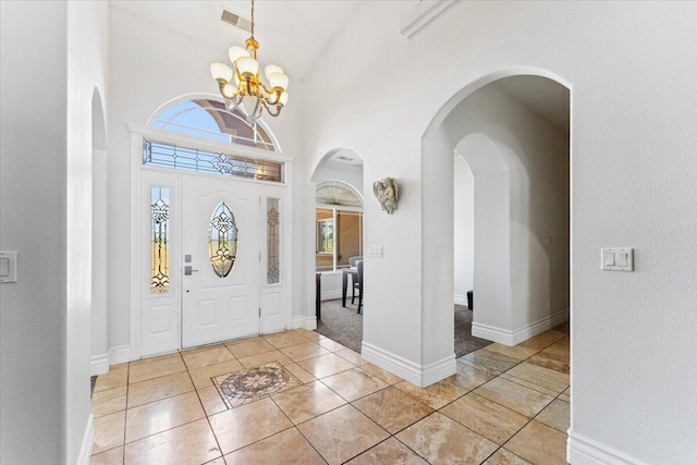 foyer entrance featuring visible vents, arched walkways, a notable chandelier, light tile patterned floors, and baseboards