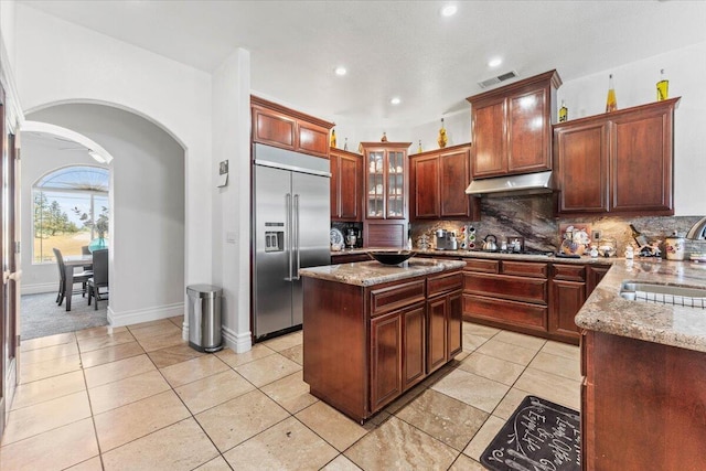 kitchen featuring under cabinet range hood, visible vents, built in fridge, a sink, and arched walkways
