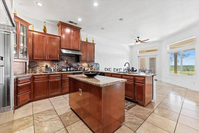 kitchen with a sink, a peninsula, visible vents, decorative backsplash, and a center island