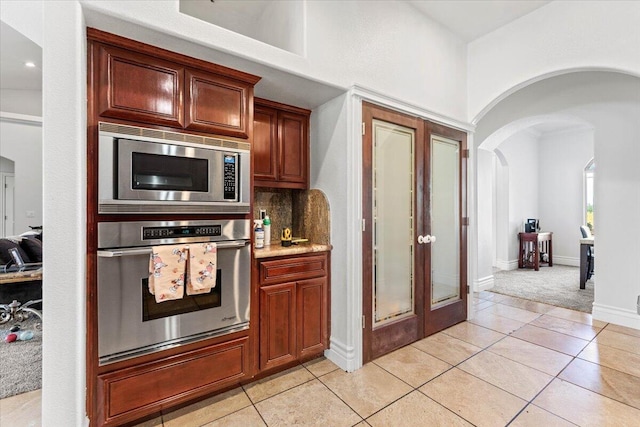 kitchen featuring stainless steel appliances, light carpet, backsplash, arched walkways, and light tile patterned floors