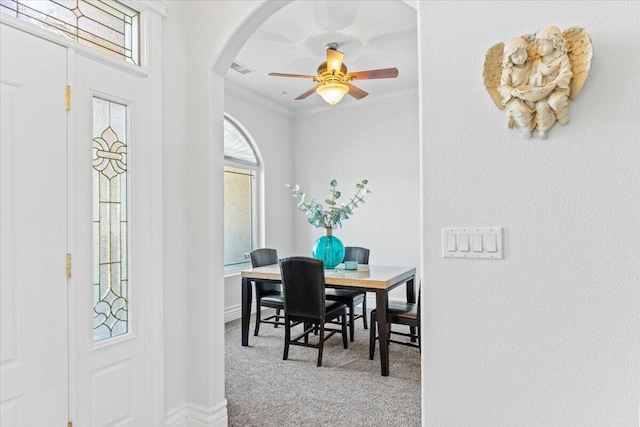 carpeted dining room featuring baseboards, ornamental molding, visible vents, ceiling fan, and arched walkways