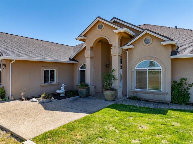 view of front facade featuring a front lawn, a shingled roof, and stucco siding