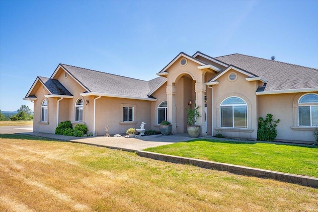 ranch-style home with roof with shingles, stucco siding, and a front yard