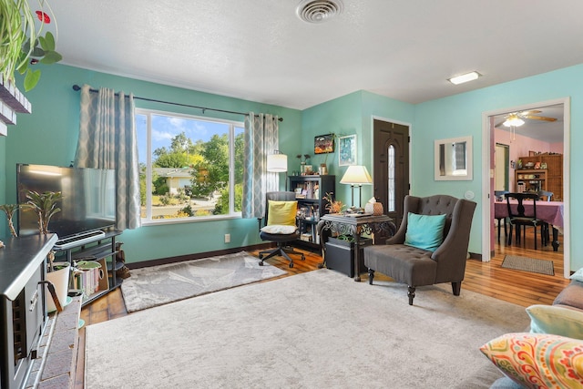 living room with baseboards, visible vents, a ceiling fan, and wood finished floors