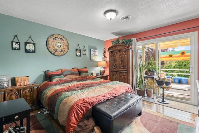 bedroom with a textured ceiling, wood finished floors, visible vents, and access to exterior