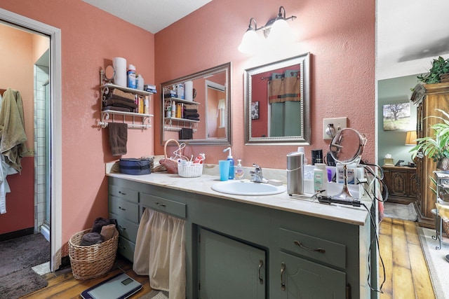 bathroom with a shower, vanity, a textured wall, and wood finished floors