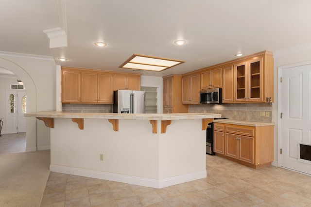 kitchen featuring stainless steel appliances, tile countertops, a breakfast bar area, crown molding, and arched walkways