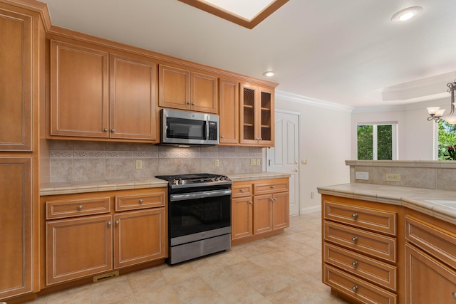 kitchen featuring glass insert cabinets, stainless steel appliances, tile counters, decorative backsplash, and ornamental molding