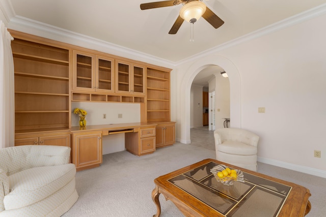 unfurnished living room with crown molding, built in desk, ceiling fan, and light colored carpet