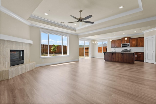 unfurnished living room featuring a premium fireplace, a raised ceiling, ceiling fan with notable chandelier, and light wood-type flooring