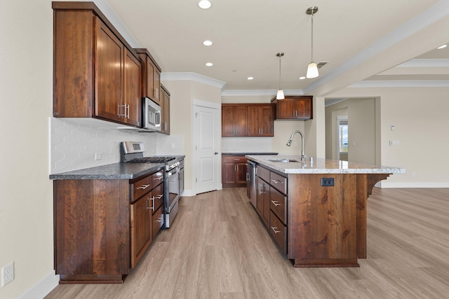 kitchen featuring appliances with stainless steel finishes, baseboards, light wood finished floors, a sink, and an island with sink