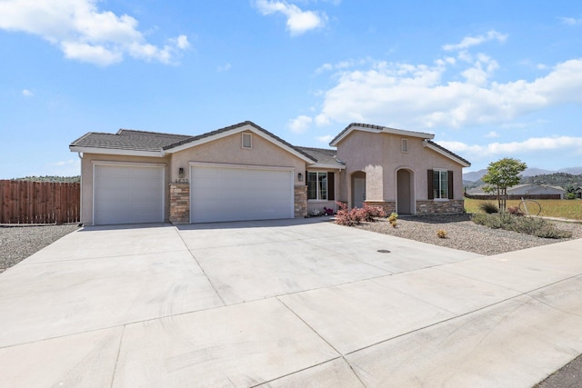 view of front of house featuring stone siding, an attached garage, stucco siding, fence, and concrete driveway