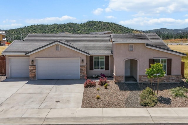single story home with a mountain view, stone siding, concrete driveway, a garage, and stucco siding