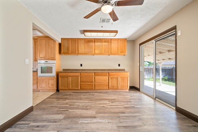1530 Carmel Way, Red Bluff, CA 96080 - kitchen with white oven, light wood-style flooring, a textured ceiling, baseboards, and ceiling fan