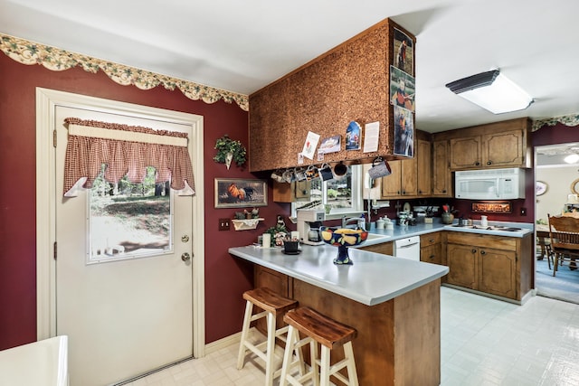 kitchen featuring a peninsula, light countertops, white appliances, a kitchen breakfast bar, and a sink