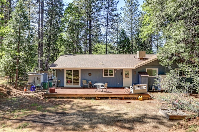 back of house featuring a storage shed, an outbuilding, a deck, a chimney, and a shingled roof