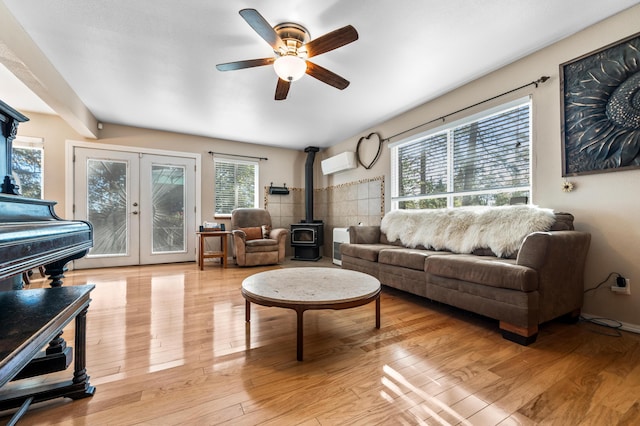 living area featuring a wood stove, an AC wall unit, ceiling fan, and wood finished floors