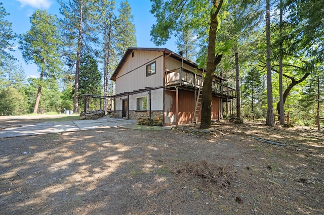view of side of home with concrete driveway, stone siding, and a deck
