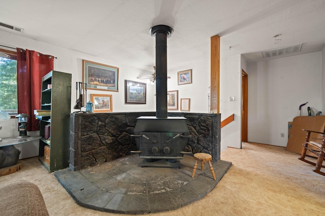 room details with carpet flooring, a wood stove, visible vents, and a ceiling fan