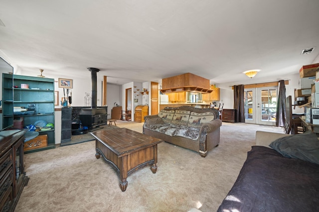 living area with a wood stove, french doors, visible vents, and light colored carpet
