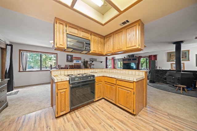 kitchen with black appliances, a wood stove, open floor plan, and tile counters