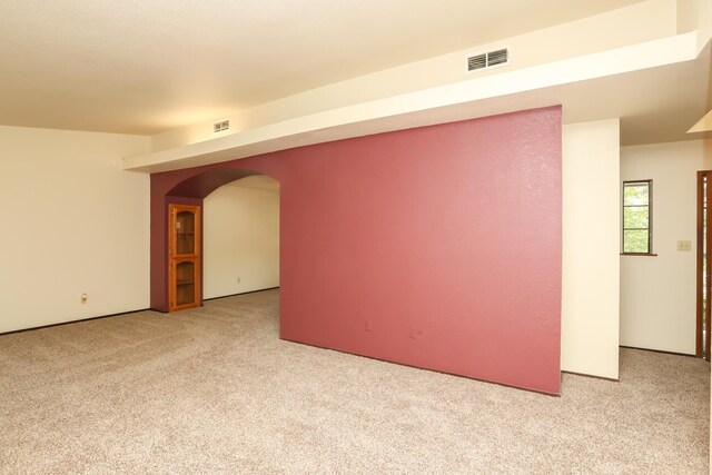 spare room featuring light carpet and arched walkways