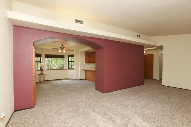 unfurnished room with light colored carpet, arched walkways, and ceiling fan