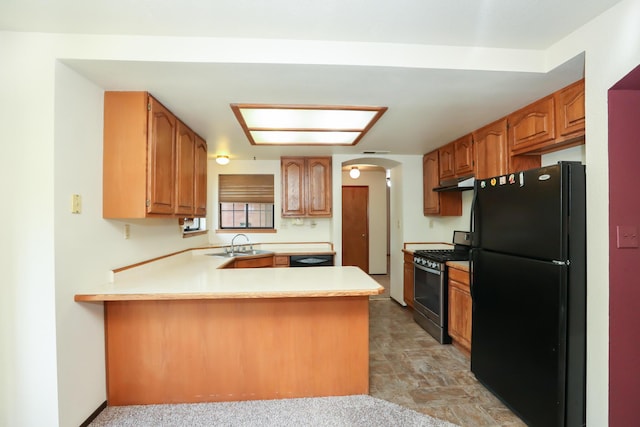 kitchen with freestanding refrigerator, stainless steel range with gas stovetop, a peninsula, arched walkways, and a sink