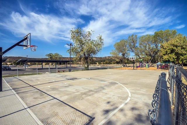 view of sport court with fence, playground community, and community basketball court