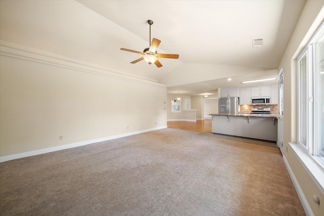 unfurnished living room featuring a ceiling fan, lofted ceiling, a wealth of natural light, visible vents, and light colored carpet