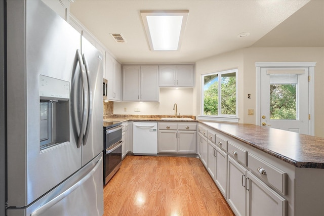 kitchen with light wood-style flooring, visible vents, a sink, a peninsula, and stainless steel appliances