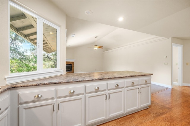 kitchen featuring a ceiling fan, light wood-style floors, a fireplace, and white cabinetry