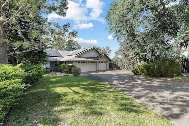 view of front facade with an attached garage, roof mounted solar panels, fence, aphalt driveway, and a front yard
