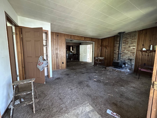 unfurnished living room featuring a wood stove, carpet flooring, and wood walls