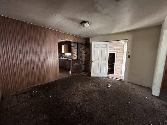 unfurnished living room featuring a wood stove, carpet, a textured ceiling, and wood walls