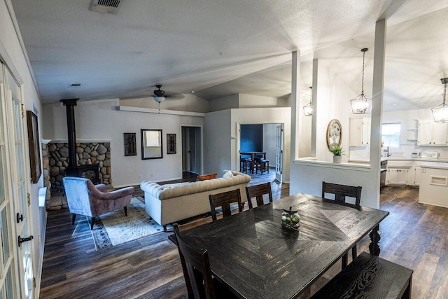 dining area featuring vaulted ceiling, a wood stove, dark wood-type flooring, and a ceiling fan