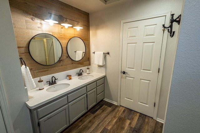 bathroom featuring wood finished floors, double vanity, a textured wall, baseboards, and wood walls