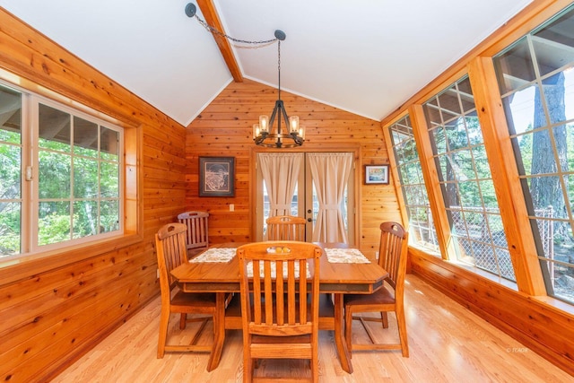 dining room with light wood finished floors, wooden walls, lofted ceiling with beams, and a notable chandelier