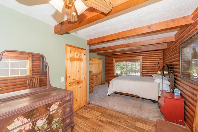 bedroom with ceiling fan, rustic walls, wood finished floors, and beamed ceiling