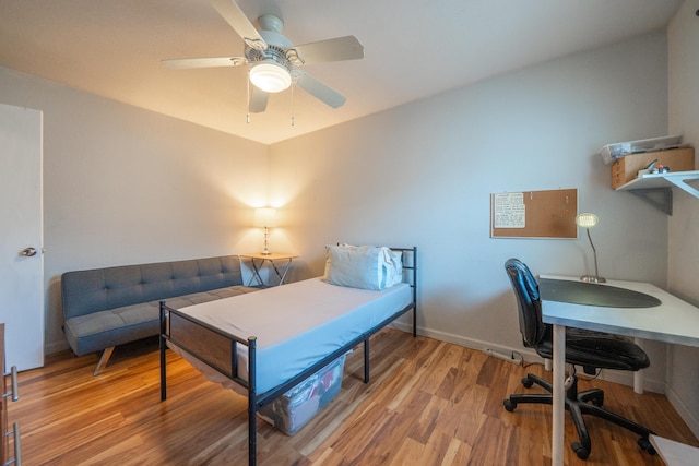 bedroom featuring wood finished floors, baseboards, ceiling fan, and a desk