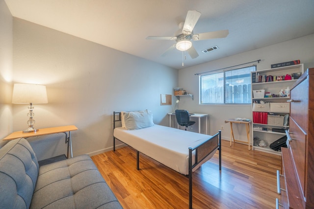 bedroom featuring wood finished floors, baseboards, ceiling fan, and a desk