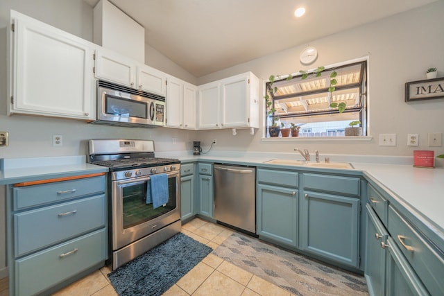 kitchen featuring appliances with stainless steel finishes, a sink, white cabinetry, vaulted ceiling, and light countertops