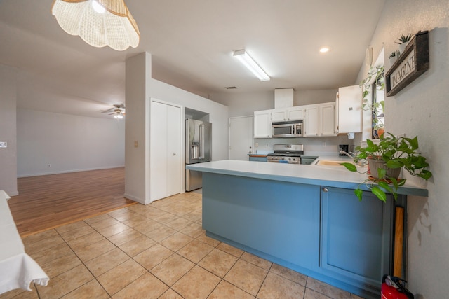 kitchen featuring appliances with stainless steel finishes, light countertops, a peninsula, light tile patterned flooring, and white cabinetry