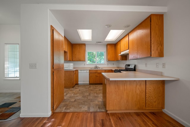 kitchen with white appliances, under cabinet range hood, a peninsula, brown cabinets, and baseboards