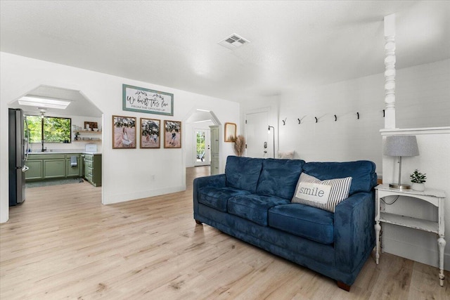 living area with arched walkways, light wood-style flooring, and baseboards