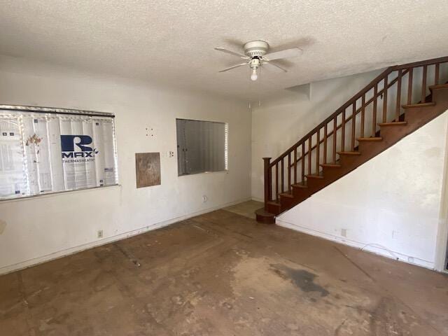 unfurnished living room featuring ceiling fan, stairway, a textured ceiling, and concrete floors