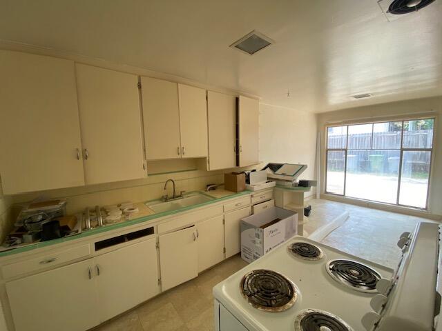 kitchen with a sink, white electric stove, and white cabinetry