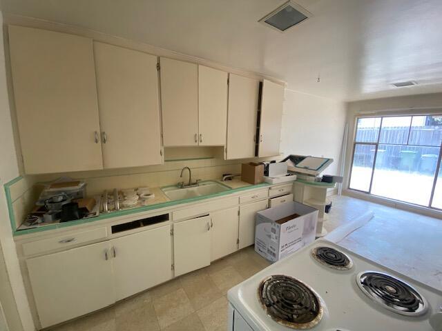 kitchen with a sink, white electric range oven, light countertops, and white cabinets