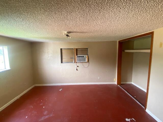 unfurnished bedroom featuring a textured ceiling, baseboards, and cooling unit